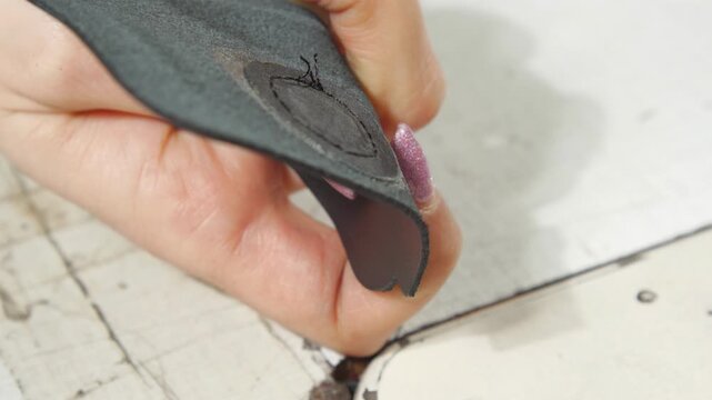 Seamstress quickly snips thread from reverse side of fabric. Woman with pink manicure trims thread with steel scissors from back of material
