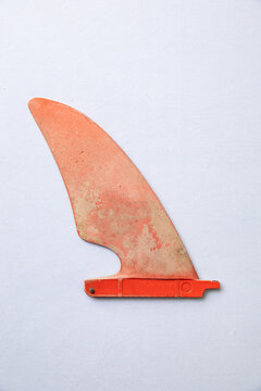 Concept for summer - old orange surfboard fin with weathered texture and a white background