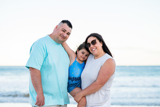 Family poses happily by the water during a beach outing on a clear day.