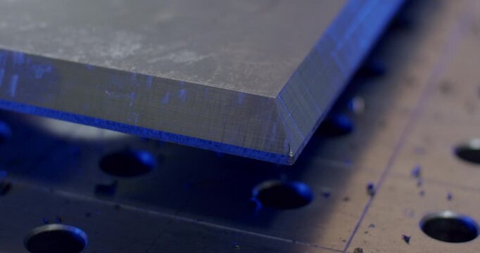 Close up of CNC machined steel part with precision cutouts and metal shavings on a professional hole grid workbench in a modern factory workshop with blue cinematic lighting for industrial engineering