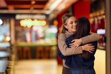 Warm Embrace Between Friends in a Modern Mall Food Court for a Joyful Reunion