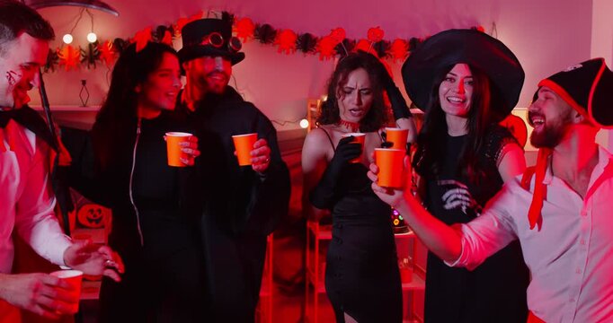 Happy Halloween holiday friends group dancing with friends wearing costumes for dress ups party night event, playing spooky horror cosplay look, garland red light decor atmosphere, entertainment