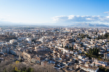 Fototapeta premium A breathtaking panoramic view of Granada stretching below the majestic Alhambra complex, with snow-capped Sierra Nevada mountains in the distance, showcasing Spain's winter tourism appeal.