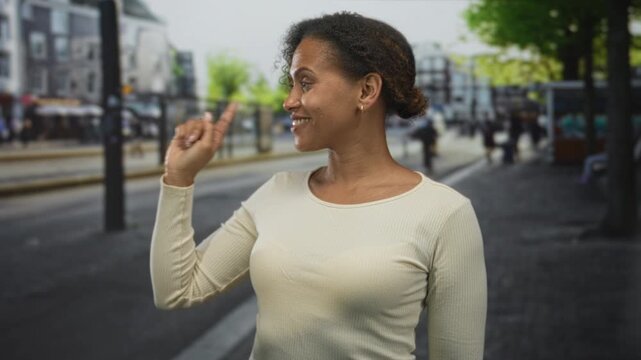 Woman points finger left on busy city street near tram shelter, smiling with raised arm and relaxed posture; confidence direction.