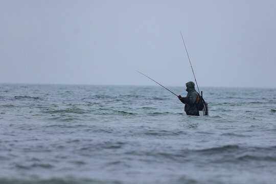 Angler steht im kalten Ostseewasser und fischt bei winterlicher Stimmung im Meer.