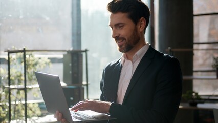 Fototapeta premium Confident Caucasian businessman typing laptop in office morning sunlight smiling professional male leader manager entrepreneur working computer executive boss indoor workplace business man guy success
