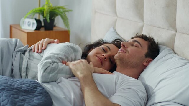 Happy Caucasian couple man woman lying on bed at home bedroom hugging together boyfriend girlfriend comfortable cozy rest relaxing embrace cuddle harmony tenderness love weekend beloved daydream sleep