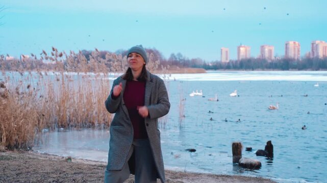 Woman performs outdoors at dusk. Outdoor stage scene with dancer and tranquil landscape background. Caucasian woman enacting emotional dance moves beside lake during winter evening illumination