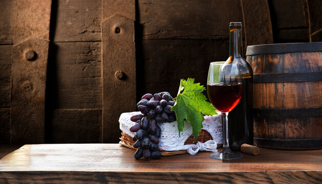 Red and white wine bottles with a grape basket on a rustic wooden table, set against a picturesque vineyard landscape. A perfect scene for wine lovers and countryside ambiance. High quality photo