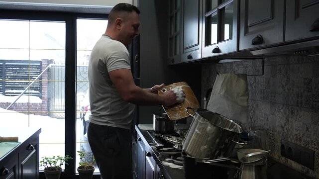 A man is washing dishes in the kitchen and dancing. The man is doing housework and having fun.