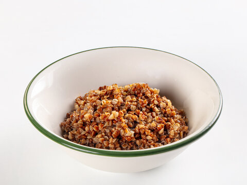 Cooked buckwheat porridge in a white bowl with a green rim, isolated on a white background