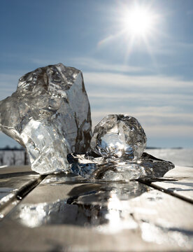 Sun shining over melting ice blocks on a wooden surface in Lithuania, symbolizing spring thaw or climate change.
