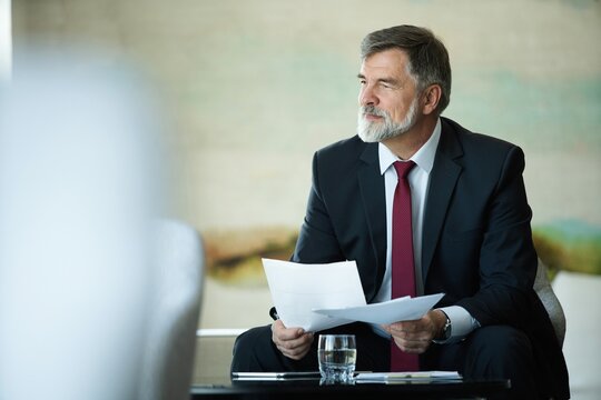 Focused serious mature businessman professional lawyer executive holding paper checking document analyzing financial report, male legal expert banker reading contract sitting at table