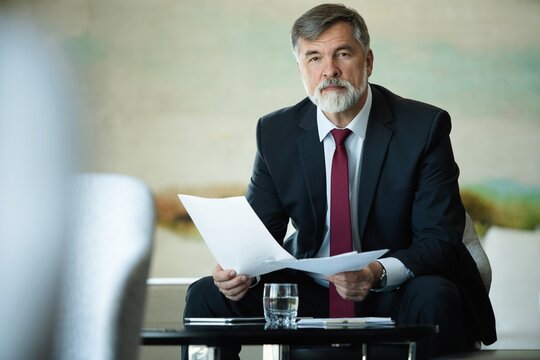 Focused serious mature businessman professional lawyer executive holding paper checking document analyzing financial report, male legal expert banker reading contract sitting at table
