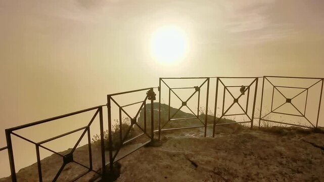 Sunrise over rocky cliff with metal railing and foggy landscape in Enna, Sicily, Italy, showcasing the serene beauty of nature at dawn