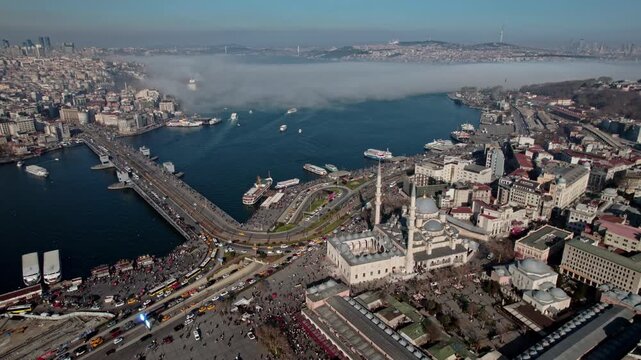 Aerial city panorama of Istanbul&rsquo;s Emin&ouml;n&uuml; district featuring the New Mosque (Emin&ouml;n&uuml;), the Galata Bridge, and the Bosphorus. Waterfront roads, ferry traffic, public square, and dense urban fabric com