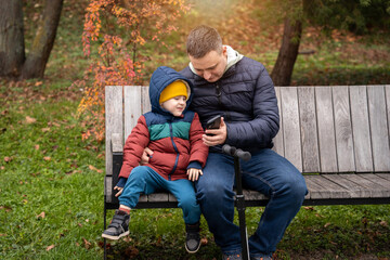Beautiful 35 year old caucasian father with toddler 4 year son sits on a bench in a city park and...
