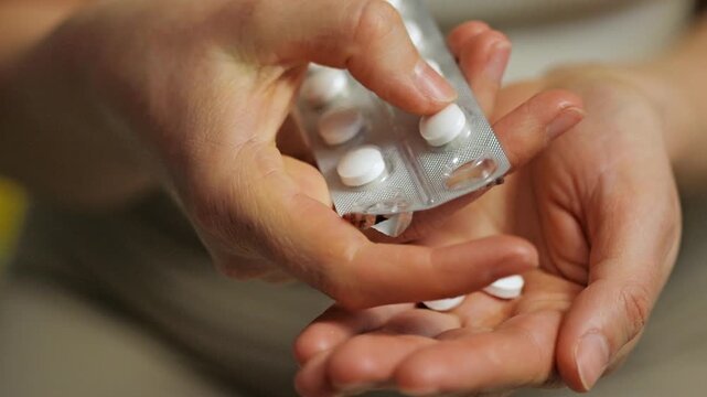 A person carefully removes white pills from a blister pack using one hand, while the other hand holds the pack. This action demonstrates medication preparation