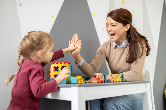 Happy female preschool teacher giving high five to a young child, celebrating a successful learning activity and promoting positive interaction in a classroom setting