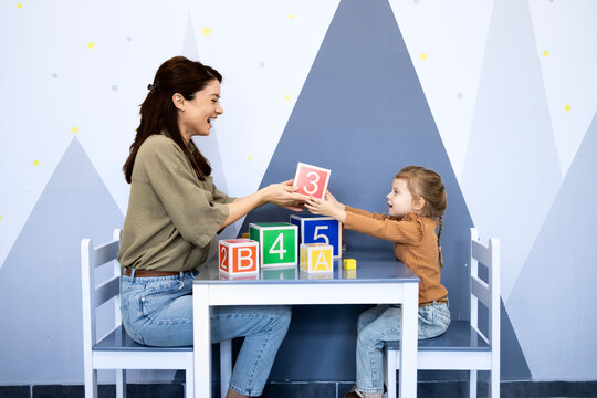 Speech therapist working with a young child developing speech and language skills using colorful alphabet and number blocks during a playful educational lesson