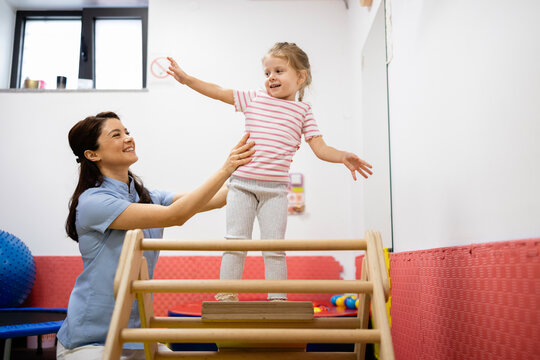 Pediatric physiatrist supporting a young girl engaging in physical therapy exercises for rehabilitation, developing motor skills, balance, and independence in a clinic