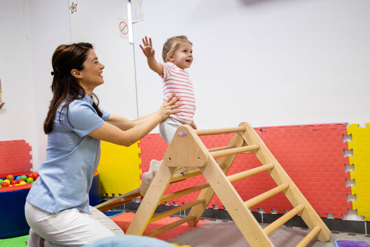 Pediatric physiatrist helping toddler during physical therapy exercise, child developing gross motor skills in rehabilitation clinic, young patient improving balance