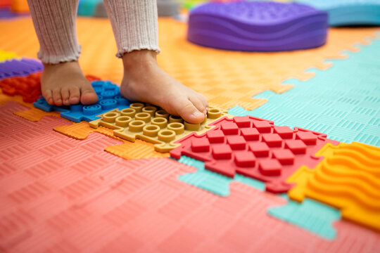 Child's bare feet stepping on colorful orthopedic sensory mat puzzles, receiving physical therapy for sensory development, balance, and flat feet prevention
