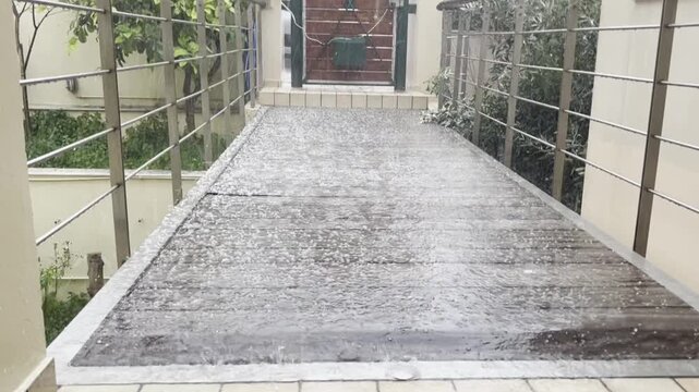 Hail falling onto wooden walkway during heavy hail shower rain storm outside residential house entrance in Greece. Ice pellets bouncing on deck surface and ground