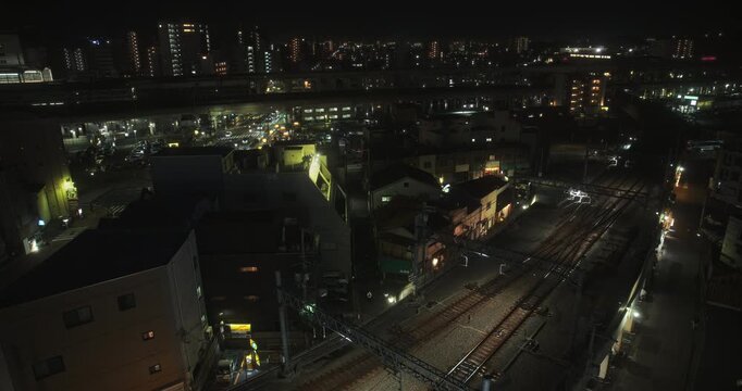 Epic high shot over Japanese city, tracks and glowing train passing by - locked off shot