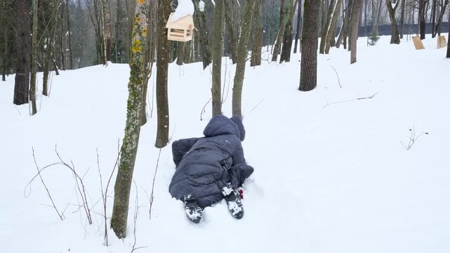 Woman crawling through deep snowdrift in winter forest, smiling and playfully moving forward despite resistance. Concept of returning to childhood, overcoming life obstacles and ironic adult struggle