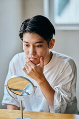 Asian young man checking his skin in mirror at home