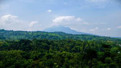 Naklejka premium Lush green mountains and dense forest under a cloudy blue sky, a breathtaking natural landscape view