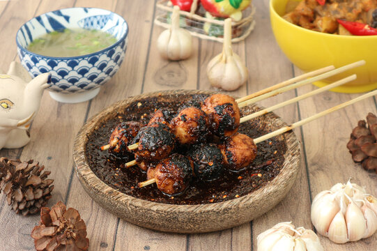 Indonesian food called bakso bakar, or grilled meatballs on skewers, served and seasoned with spicy sweet soy sauce..