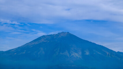 Imposing mountain peak standing tall against a clear blue sky dotted with soft clouds, showcasing the serene and powerful beauty of a natural landscape vista