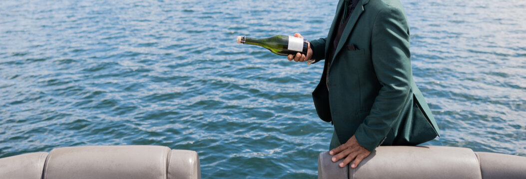 Hombre elegante sosteniendo botella de champ&aacute;n en yate frente al mar