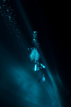 View of a diver descending into the deep blue, illuminated by shafts of light piercing the darkness in Tulum, Quintana Roo, Mexico.