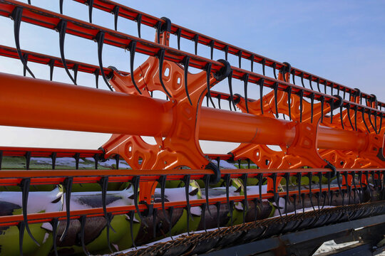 A detailed close-up of a bright orange combine harvester header showcases the complex design of metal teeth and mechanisms.