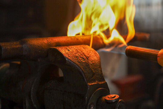 A powerful gas burner flame heats a massive metal part clamped in steel vices within a professional workshop. This shot demonstrates the intensive process of thermal metal treatment, conveying the atm