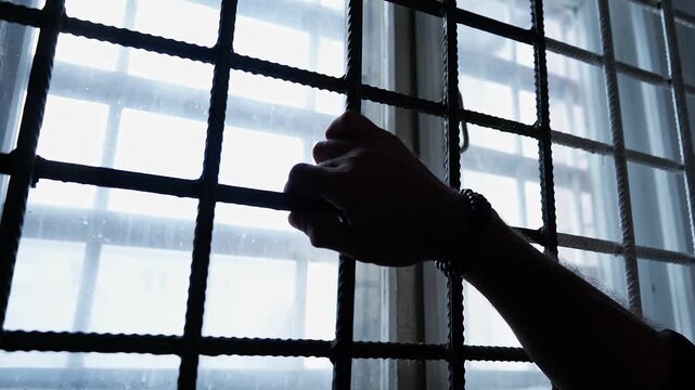 Close-up of Hand Gripping Metal Bars on Window with Bright Light