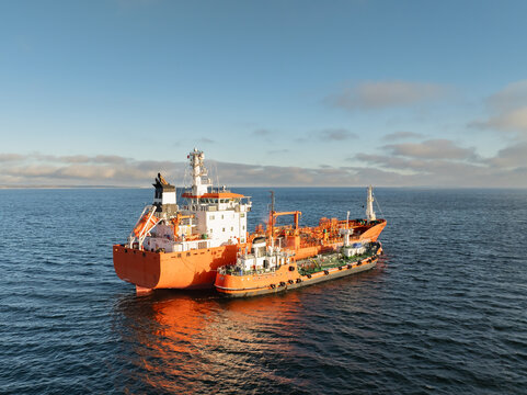 Aerial drone view of orange chemical tanker ship bunkering and refueling from a smaller bunker vessel in the Baltic Sea