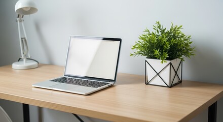 Fototapeta premium Laptop and plant sit on a wooden desk in a simple room setup during daytime hours