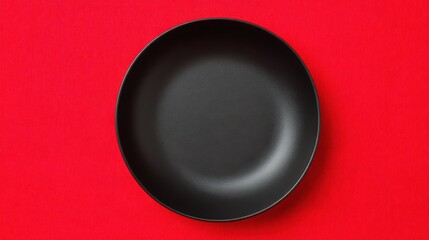 top view of empty matte black dessert plate on vibrant red tablecloth, minimal composition, strong color contrast, clean space, modern food styling