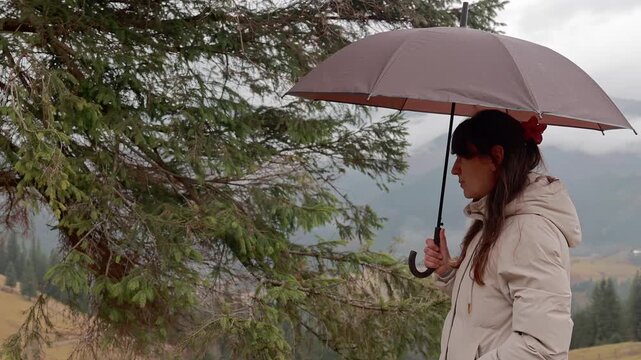 Profile of a woman with red umbrella looking at misty mountain valley, peaceful morning in the carpathians with low clouds and forest scenery