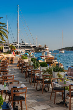 View of sun-drenched tables and chairs line the waterfront, with luxury yachts bobbing gently on the azure sea, reflecting the clear sky, Grad Hvar, Splitsko-dalmatinska zupanija, Croatia.