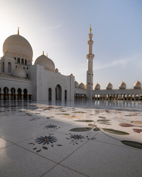 View of the grand mosque with its white domes and minarets reflecting on patterned marble floors under a bright sky, Al Rawdah, United Arab Emirates.