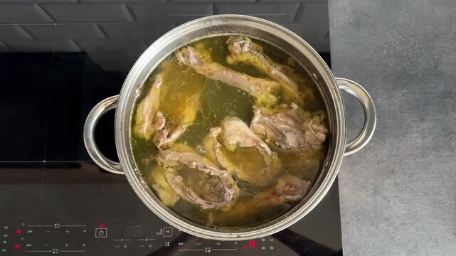 Cooking healthy bone broth with chicken backs and turkey bones. Boiling nutrient-dense bouillon in a stainless steel pot. Natural source of collagen and minerals for keto and paleo diet.