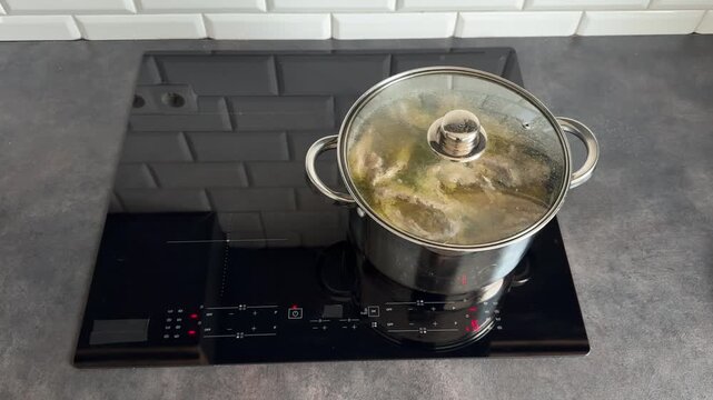 Boiling homemade soup with chicken and turkey in a stainless steel pot. Close up of rich golden bouillon simmering on an induction stove. Healthy nutrient-dense meal preparation.