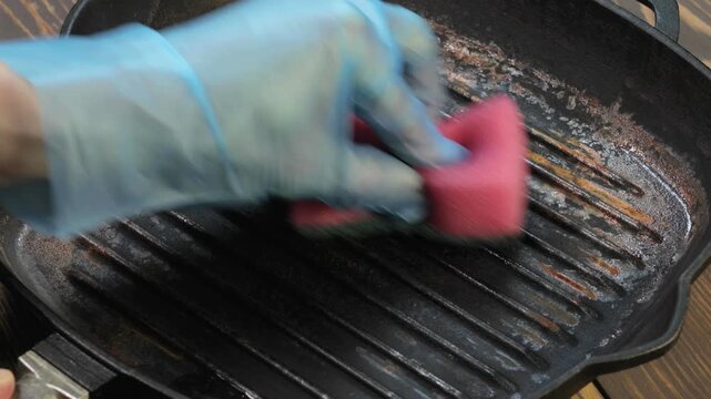 Hand clean rusted cast iron frying pan with sponge. Burnt pot with black bottom. Pan burnt from cooking. Close up.