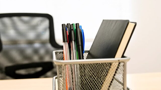 Office supplies, including pens and a notebook, are neatly arranged in a l mesh container on a desk.