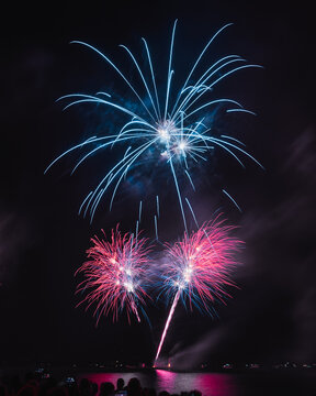 View of vibrant fireworks paint the night sky with dazzling bursts of color reflected on the serene waters below, illuminating the silhouette of the city, Neuchatel, Neuchatel, Switzerland.